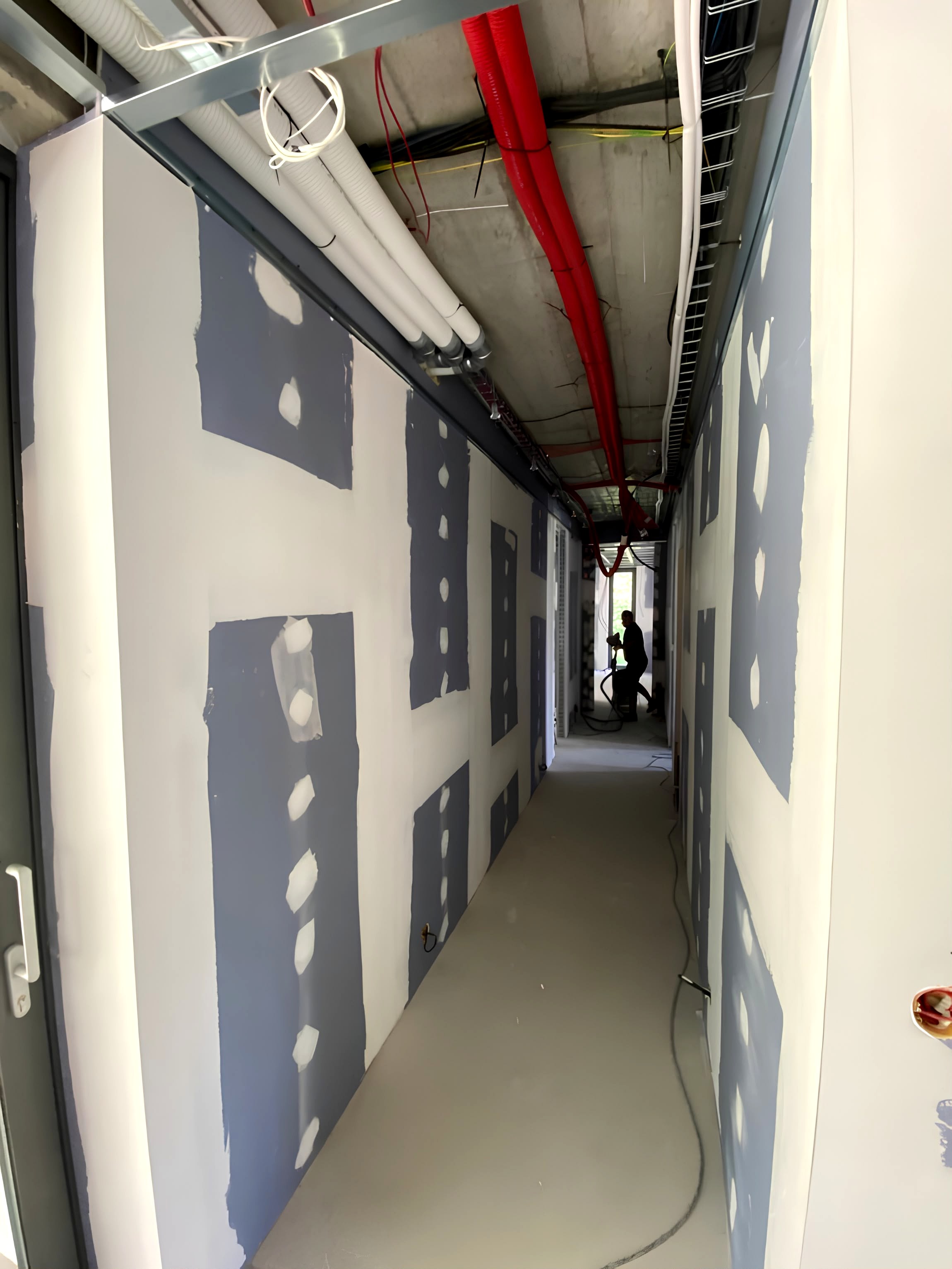 Antes · Pasillo de vivienda con trasdosado emplastecido e instalaciones eléctricas y fontanería a la vista en zona superior