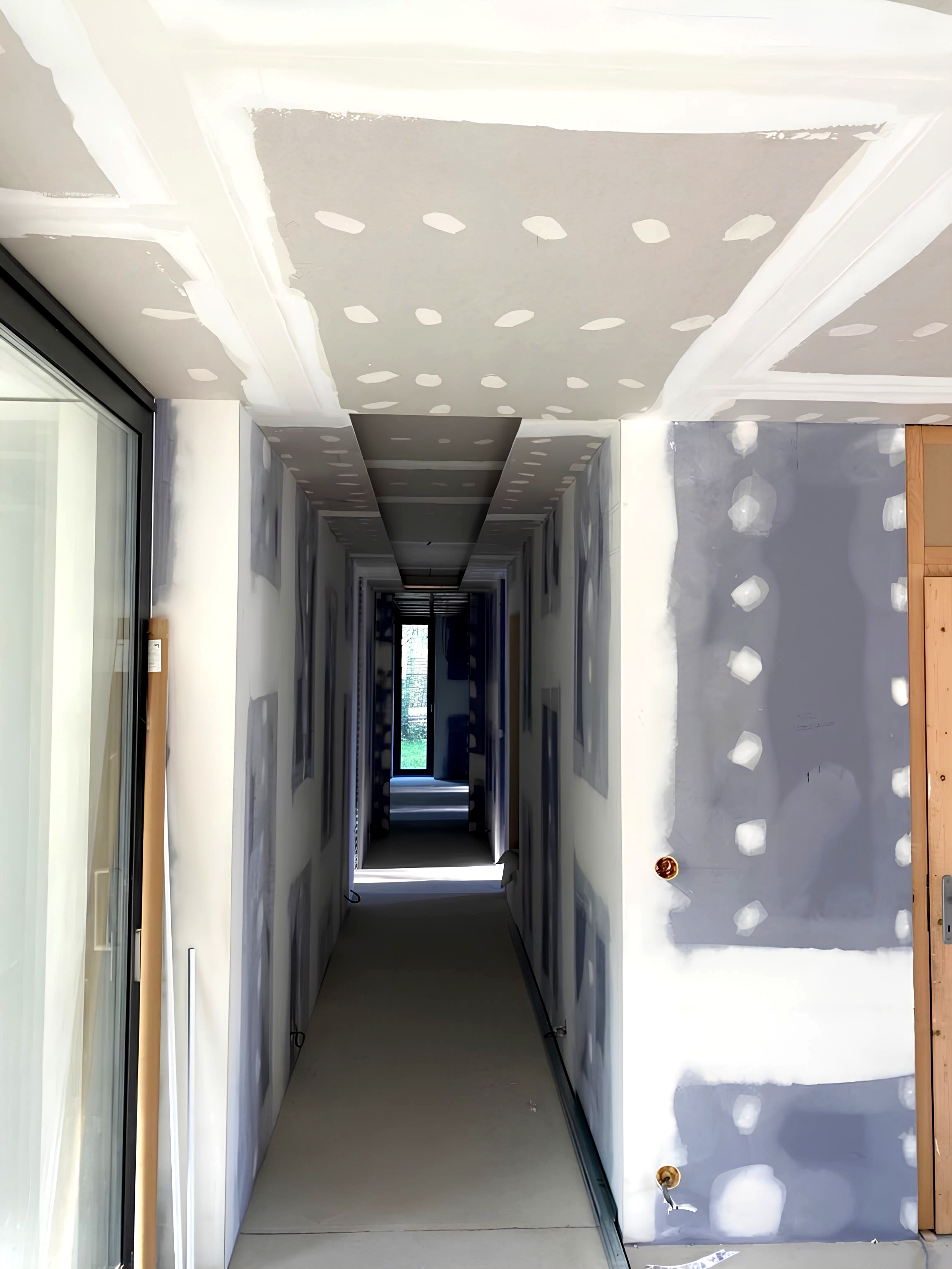 Pasillo de vivienda en Gran Canaria con techo continuo PYL emplastecido y trasdosado, luz natural al fondo